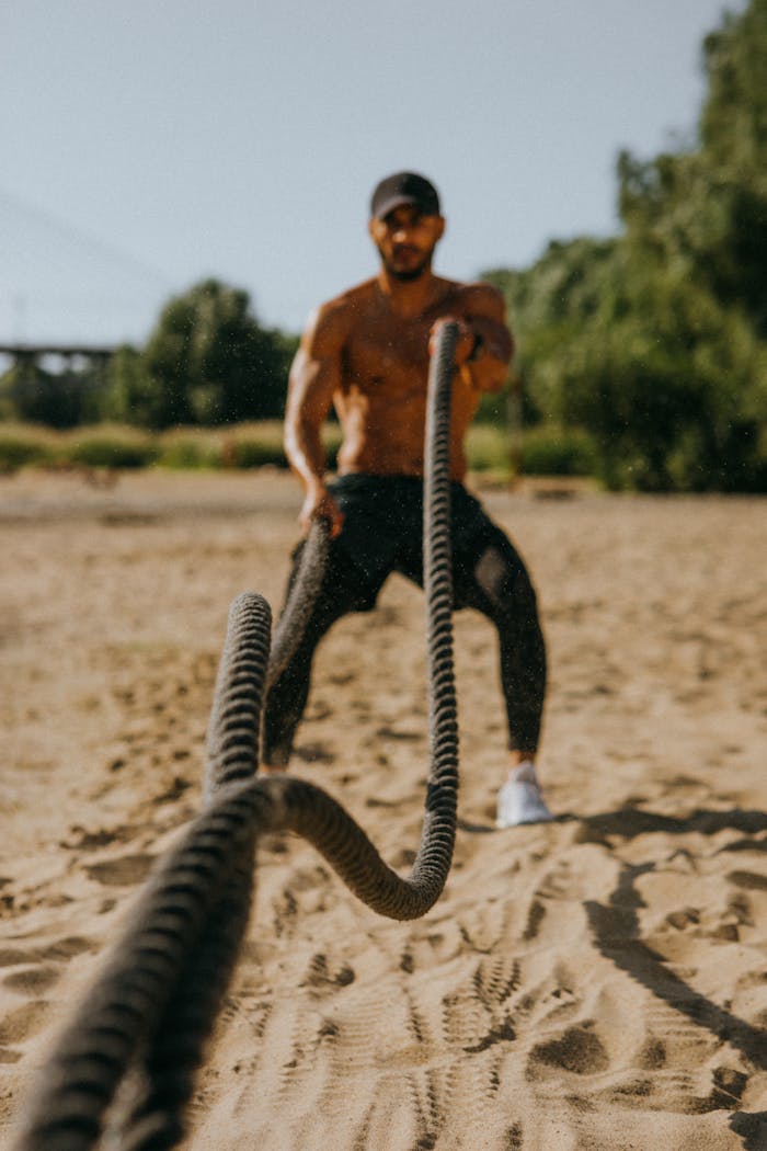 Fit man training with battle ropes on a sandy outdoor area, showcasing strength and endurance.